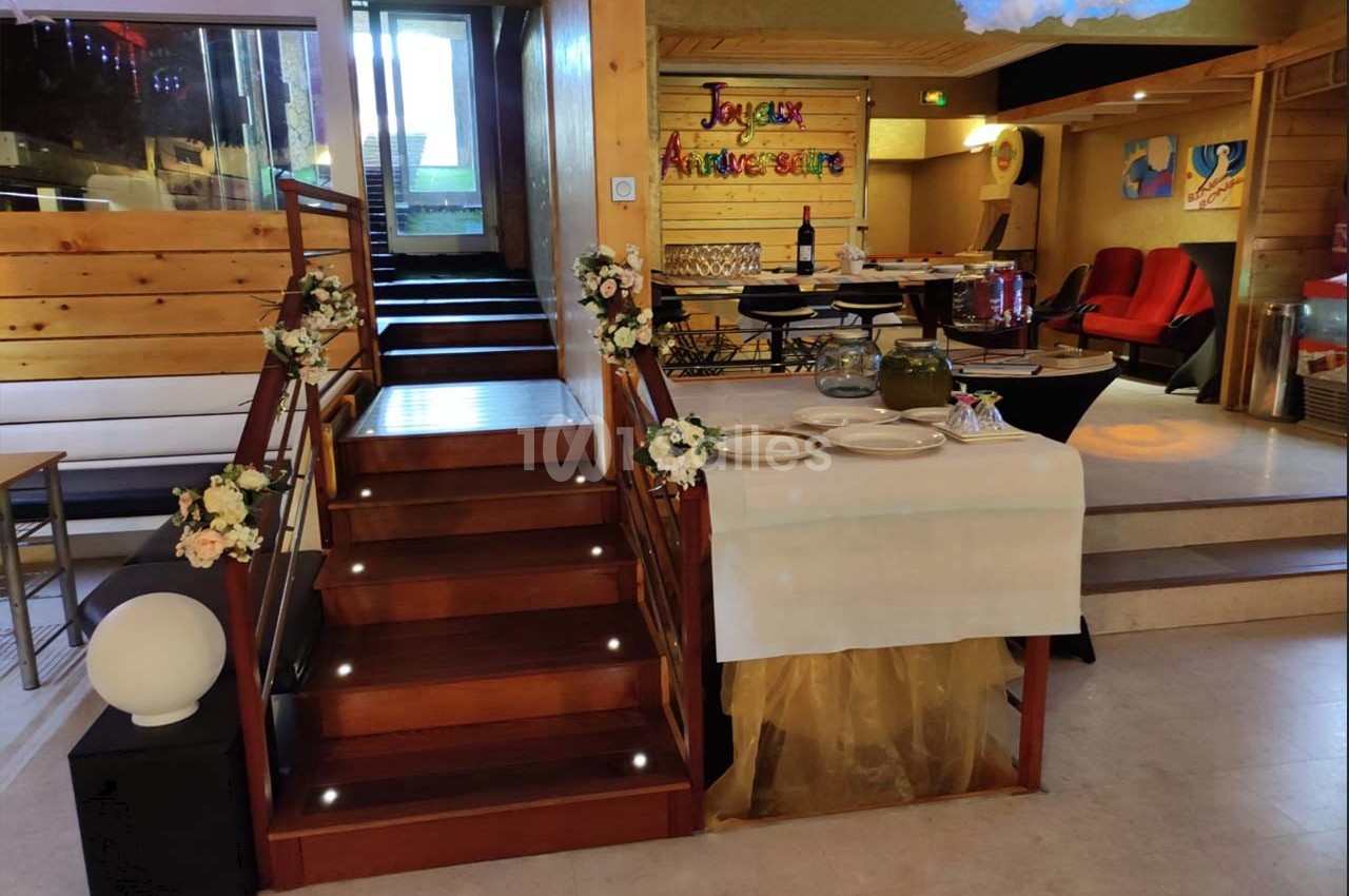 Escalier en bois décoré de fleurs, table dressée avec vaisselle et buffet, panneau ’Joyeux Anniversaire’ en arrière-plan.