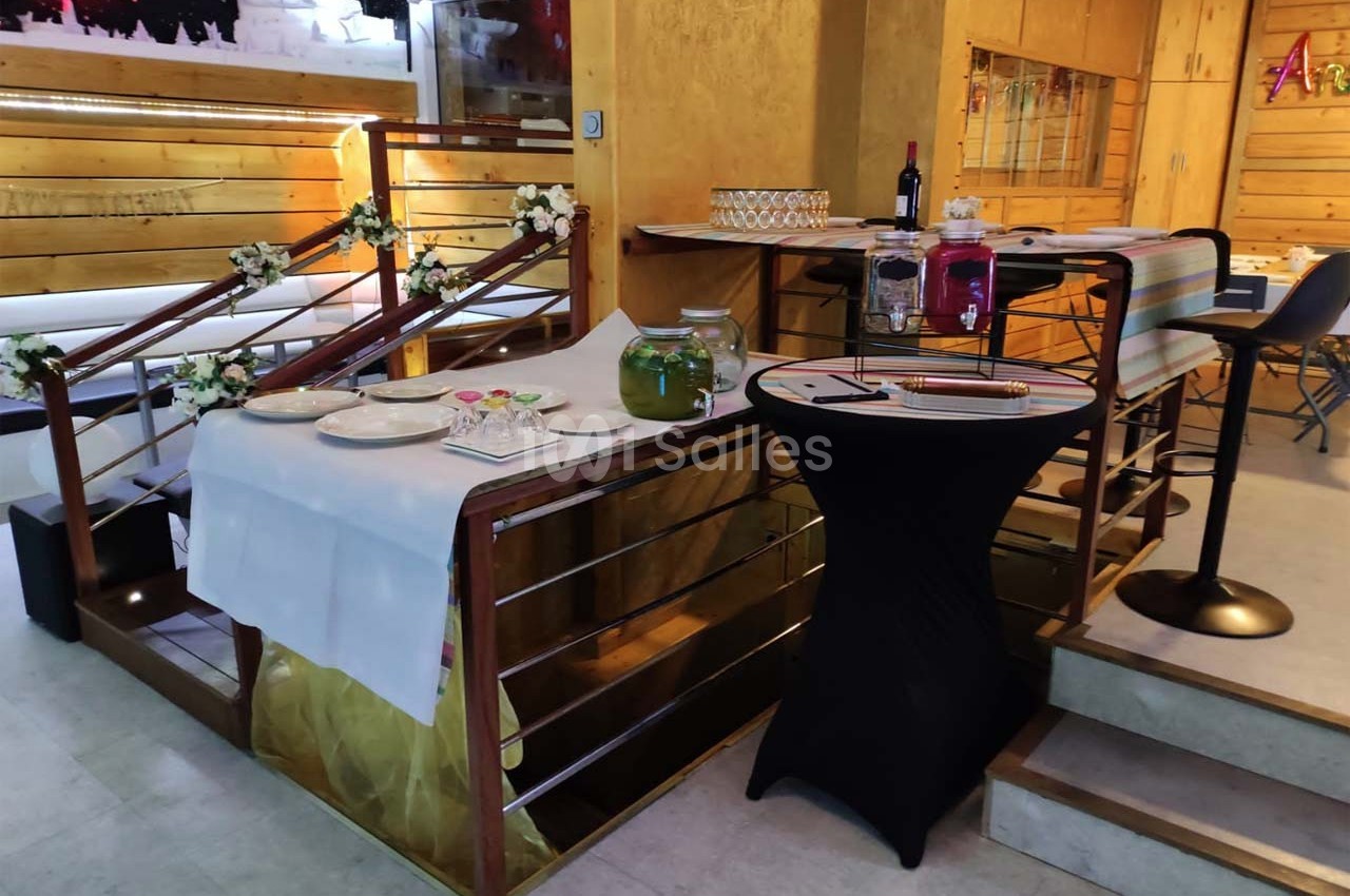Table décorée avec nappes blanches, fleurs et vaisselle, située près d'un escalier en bois dans un espace intérieur.