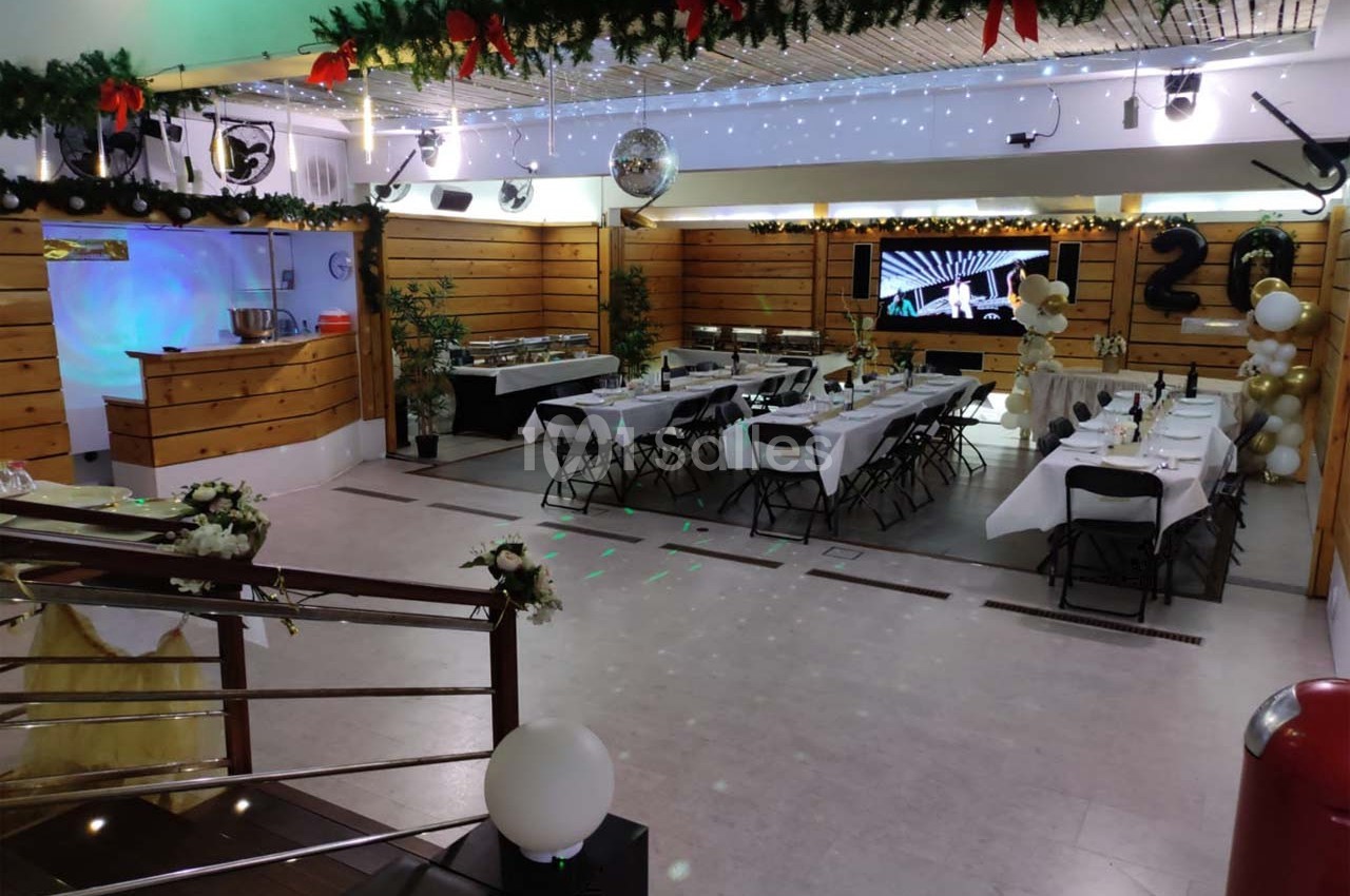 Salle décorée pour une réception, avec tables dressées, guirlandes suspendues et éclairage festif.