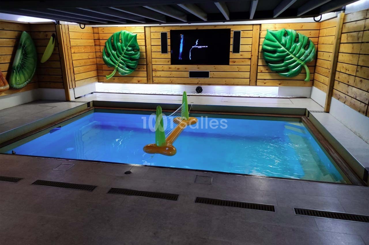 Piscine intérieure entourée de murs en bois, décorée de bouées en forme de feuilles et d'un écran mural.