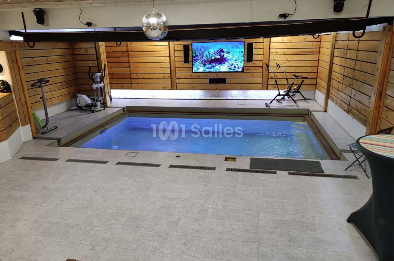 Salle intérieure avec piscine, équipements de sport, murs en bois et écran affichant une image sous-marine.
