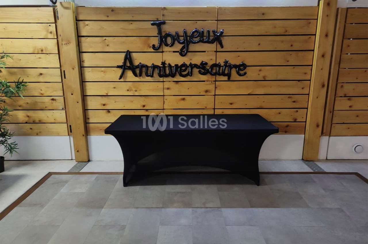 Mur en bois décoré avec l'inscription ’Joyeux Anniversaire’ et une table noire recouverte d'une nappe devant.