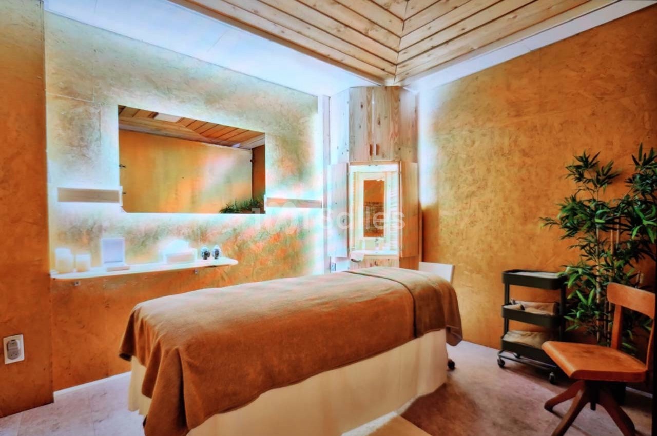 Salle de massage avec table recouverte d'un drap beige, éclairage doux et décoration en bois et plantes.