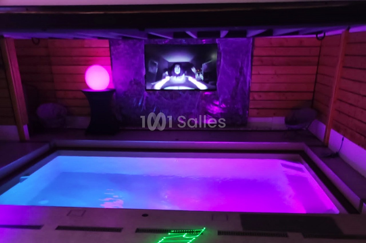 Piscine intérieure éclairée par des lumières colorées avec un écran diffusant une vidéo en arrière-plan.