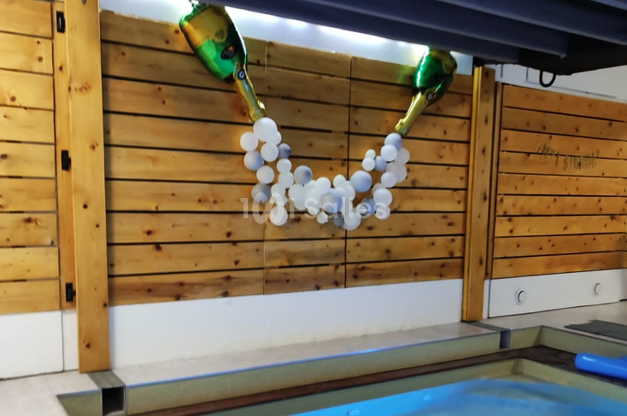 Décoration murale avec deux bouteilles factices de champagne et une guirlande de ballons blancs, près d'une piscine.
