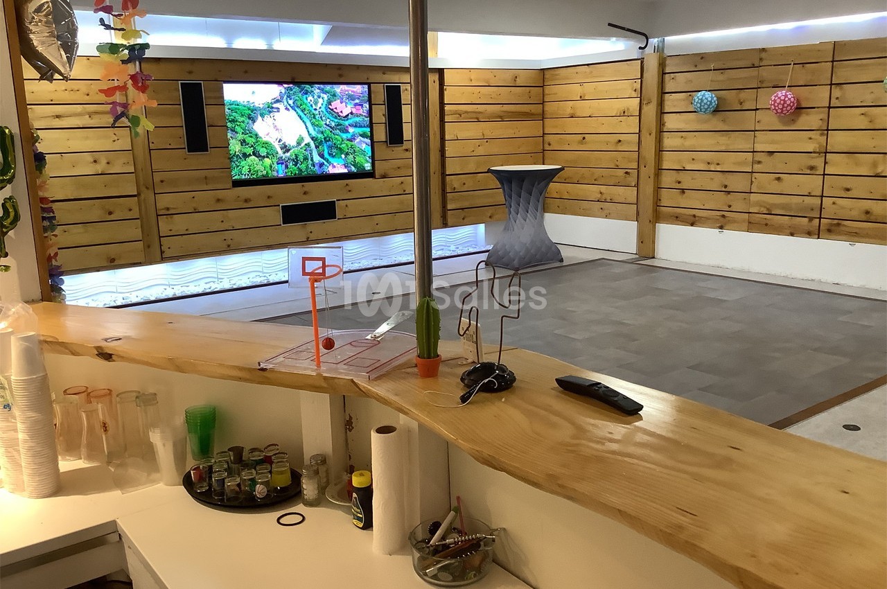 Salle avec murs en bois, écran mural allumé, comptoir au premier plan et décoration colorée.