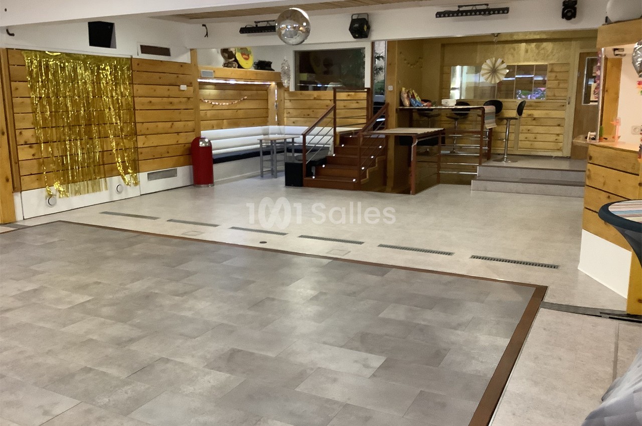 Salle vide avec parquet, murs en bois, décorations dorées et une boule disco suspendue au plafond.