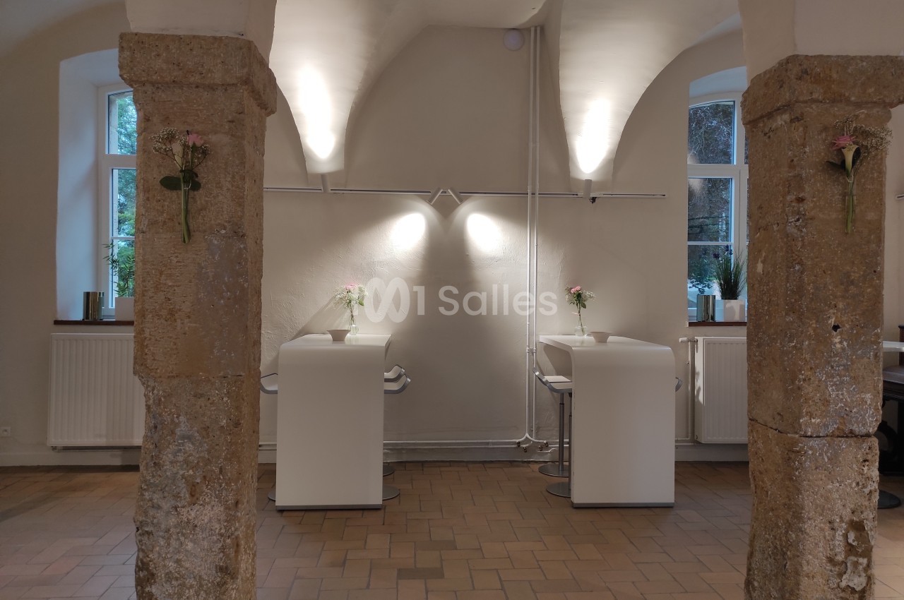 Deux colonnes en pierre encadrent un espace avec deux bureaux modernes, éclairés par des lampes murales.