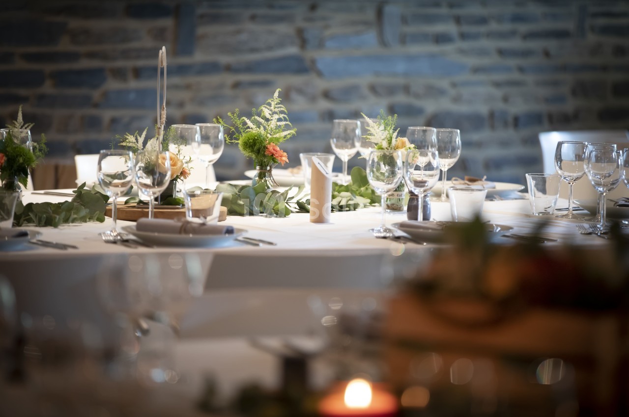Table élégamment dressée avec des verres, assiettes et décorations florales sur fond de mur en pierre.