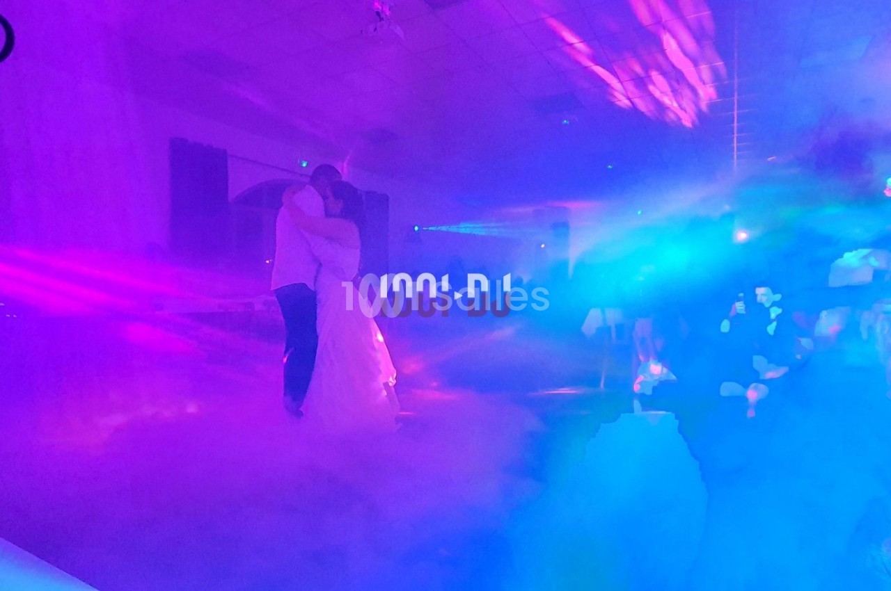 Un couple danse dans une salle éclairée par des lumières colorées et entourée de fumée.