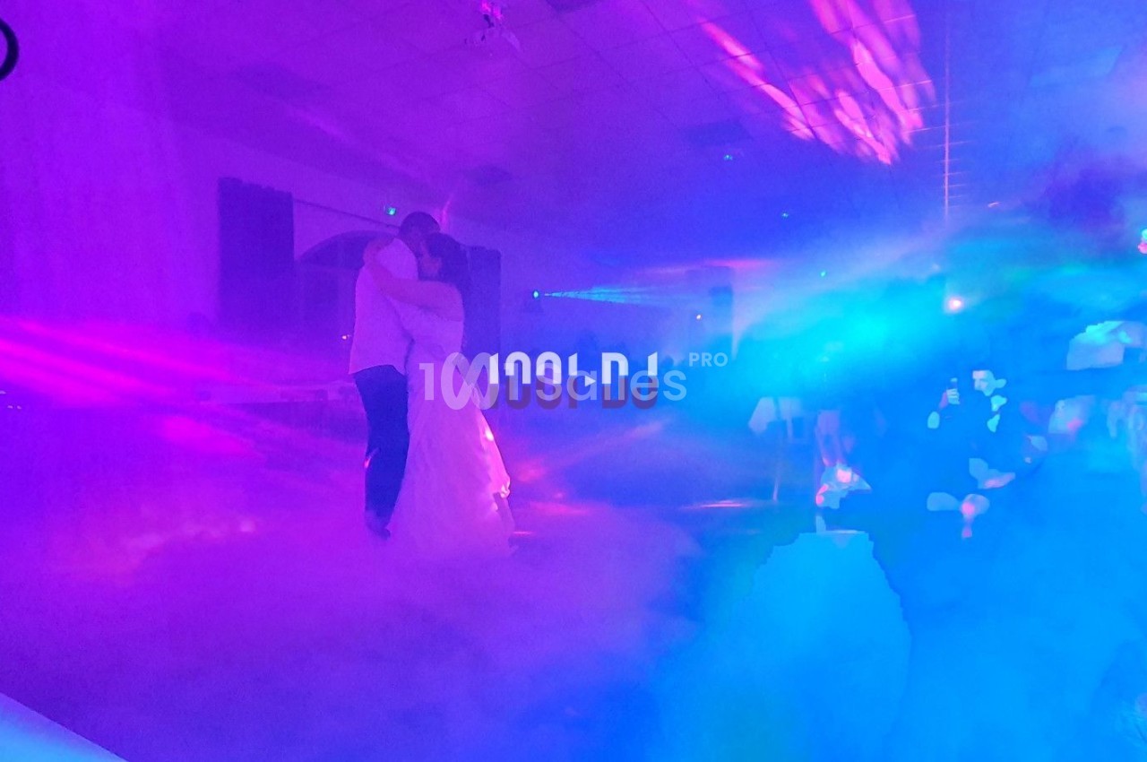 Un couple danse dans une salle éclairée par des lumières colorées et entourée de fumée.