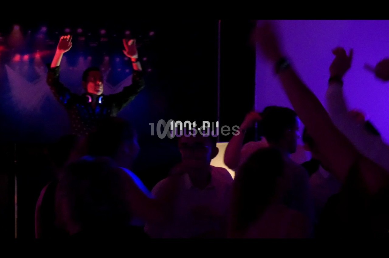 Un DJ anime une soirée dansante avec des lumières colorées et une foule en mouvement.