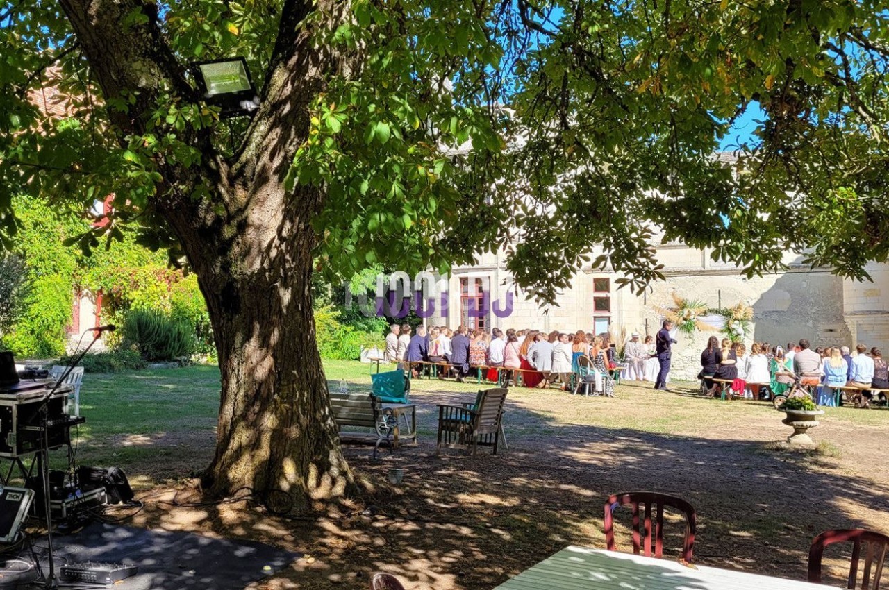 Un groupe de personnes assises à l'extérieur sous des arbres, près d'un bâtiment, avec du matériel audio visible au premier…
