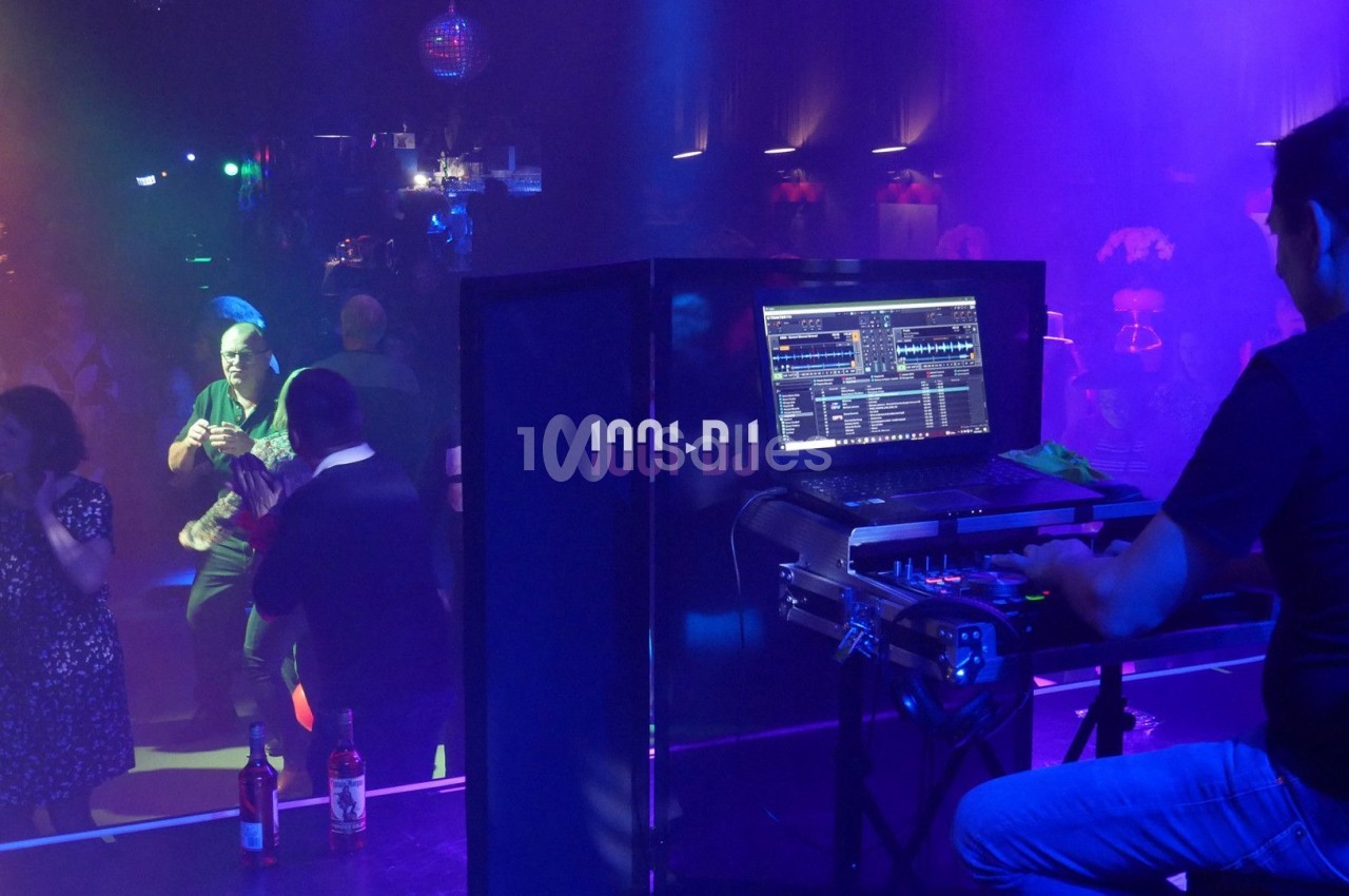 Un DJ mixe sur scène dans une boîte de nuit, avec des lumières colorées et des danseurs sur la piste.