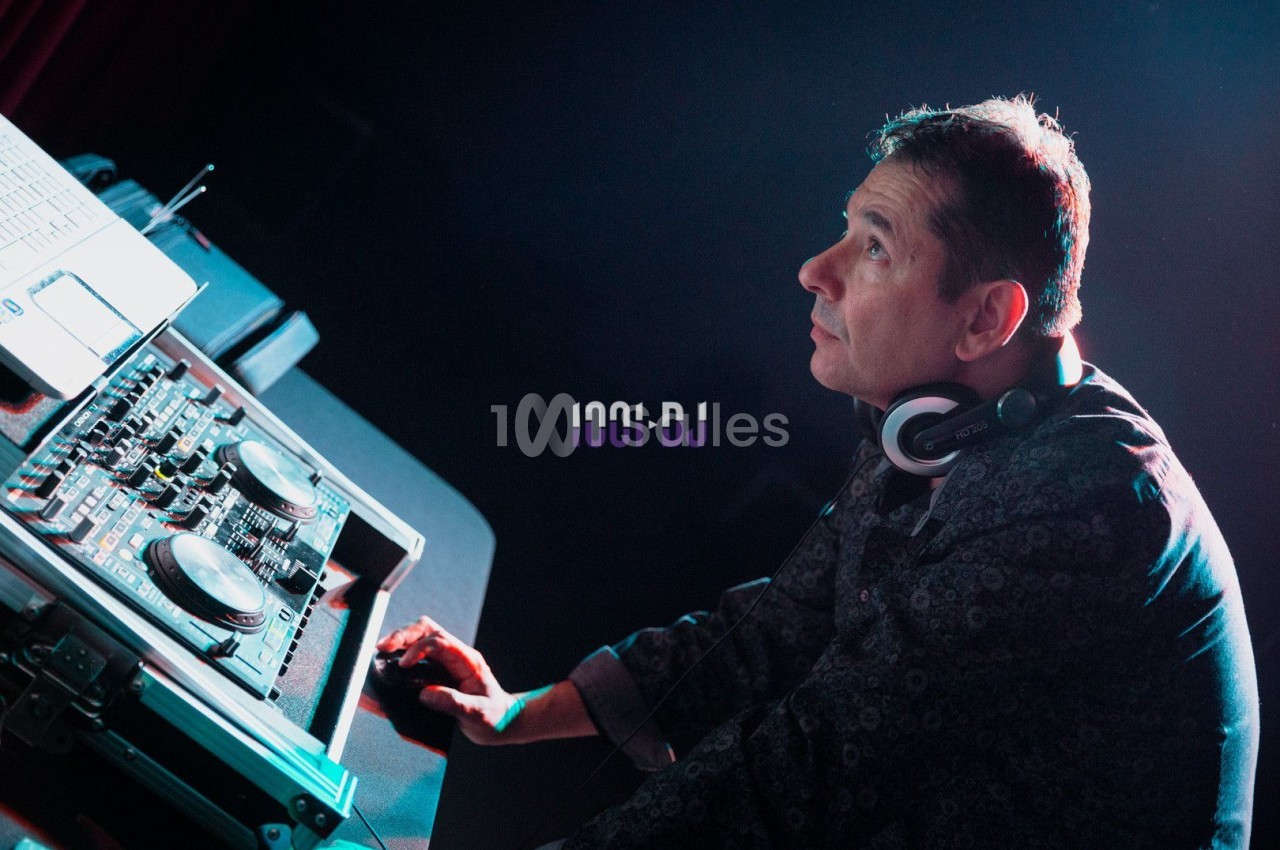 Un DJ portant un casque audio utilise une table de mixage dans une ambiance lumineuse tamisée.