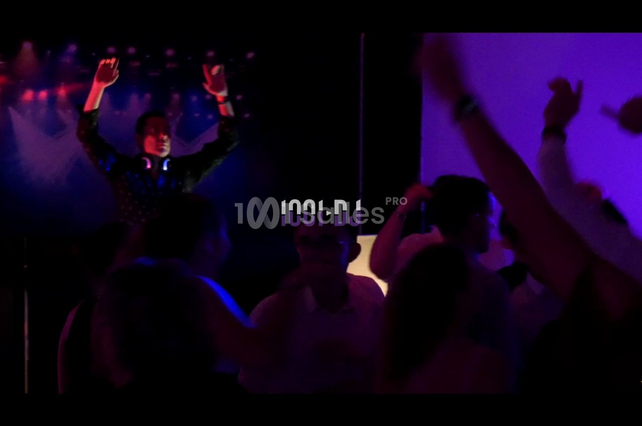 Un DJ anime une soirée dansante avec des lumières colorées et une foule en mouvement.
