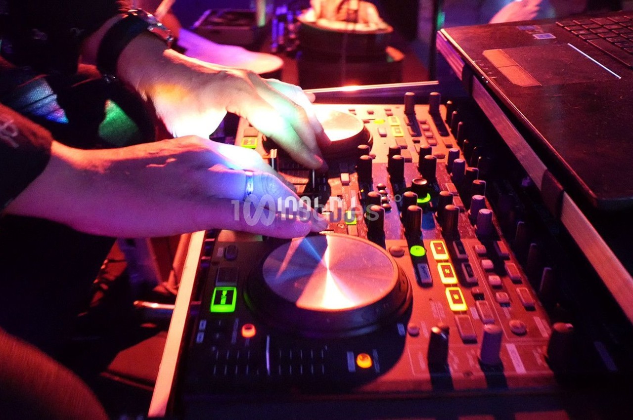 Mains manipulant une table de mixage audio éclairée par des lumières colorées dans un environnement sombre.