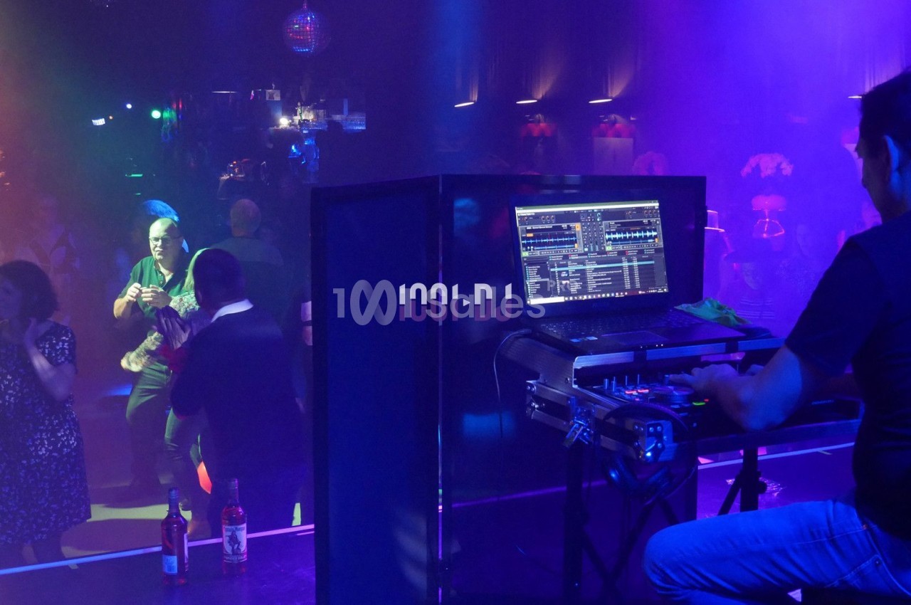 Un DJ mixe sur scène dans une boîte de nuit, avec des lumières colorées et des danseurs sur la piste.