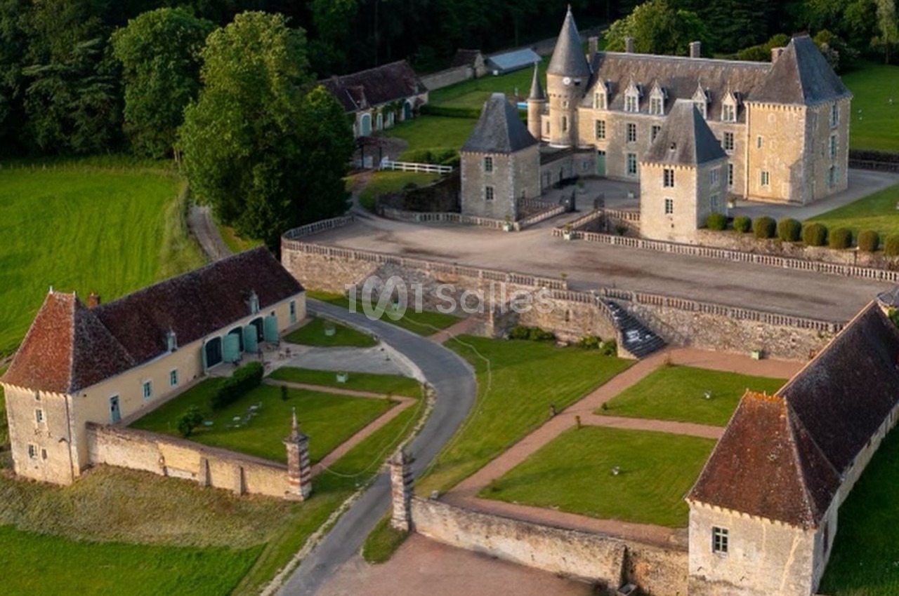 Vue aérienne d'un château historique entouré de jardins, de bâtiments annexes et de verdure.