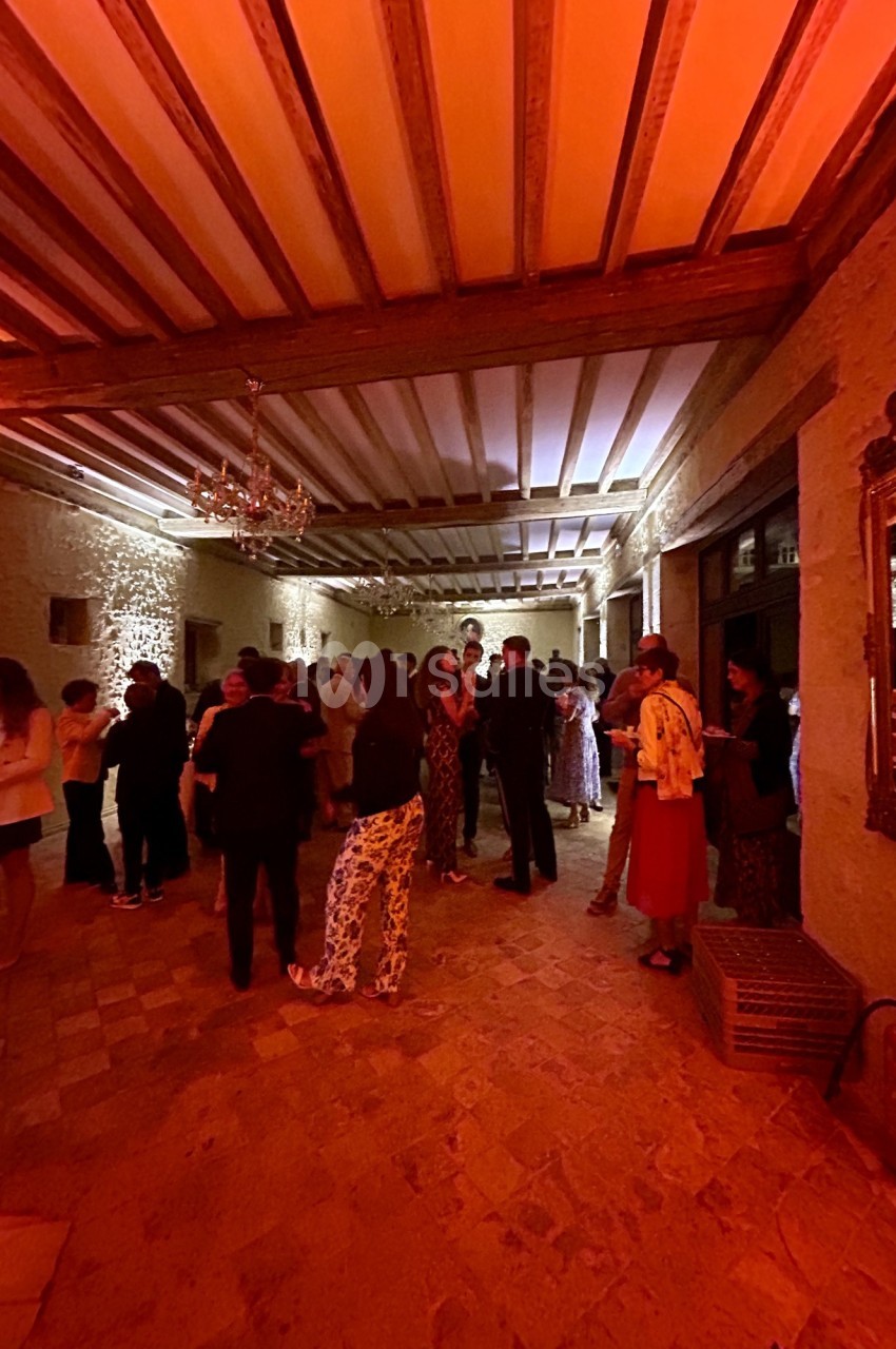 Groupe de personnes discutant dans une grande salle éclairée par une lumière chaude, avec plafond à poutres apparentes.
