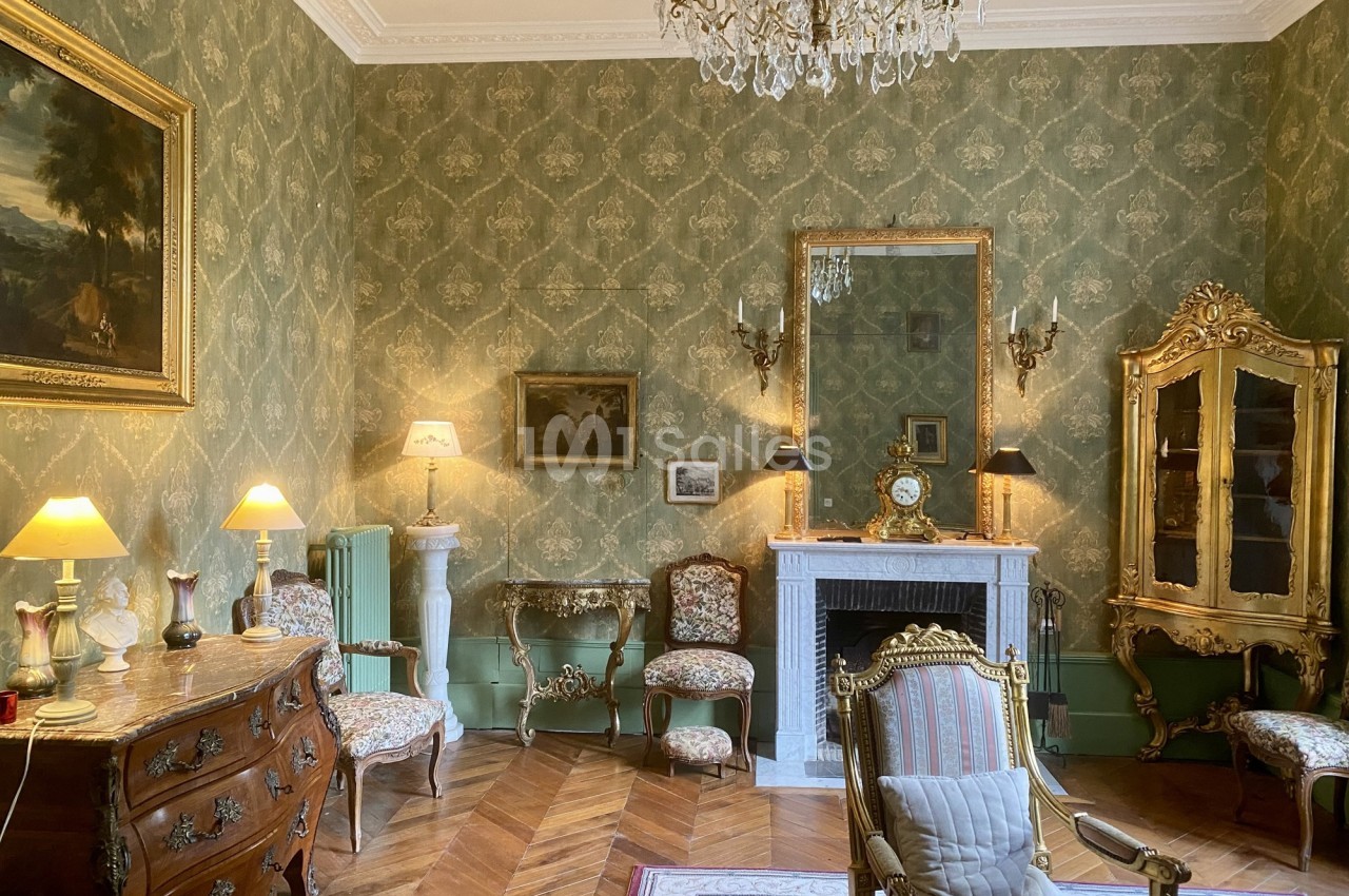 Salon élégant avec mobilier ancien, cheminée en marbre, lustre en cristal et murs ornés de papier peint vert.
