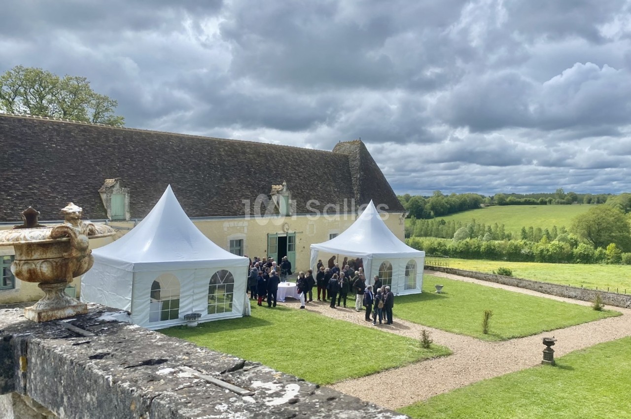 Groupe de personnes rassemblées près de tentes blanches dans la cour d'un bâtiment ancien entouré de verdure.