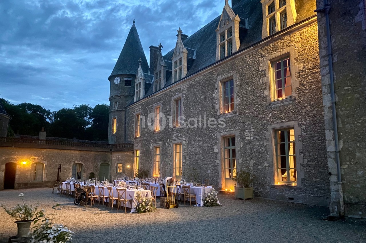 Dîner en plein air devant un château illuminé au crépuscule, avec des tables dressées et décorées.