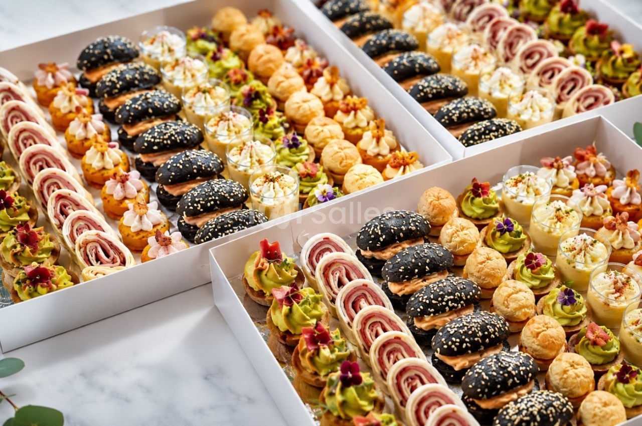 Plateaux de bouchées apéritives variées comprenant mini-burgers, roulés, choux et verrines, présentés sur une table.