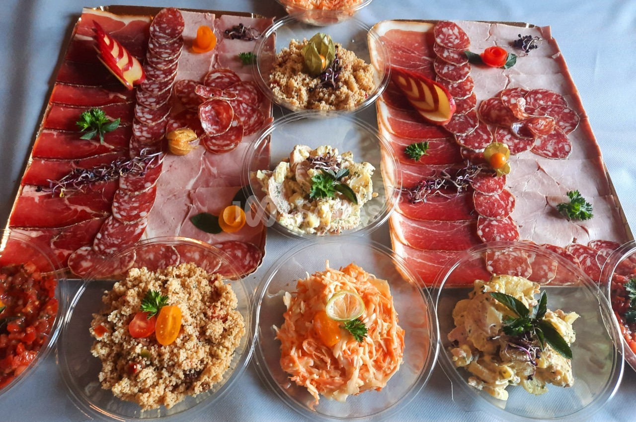 Plateau de charcuterie variée entouré de salades composées, présenté sur une table avec décoration soignée.