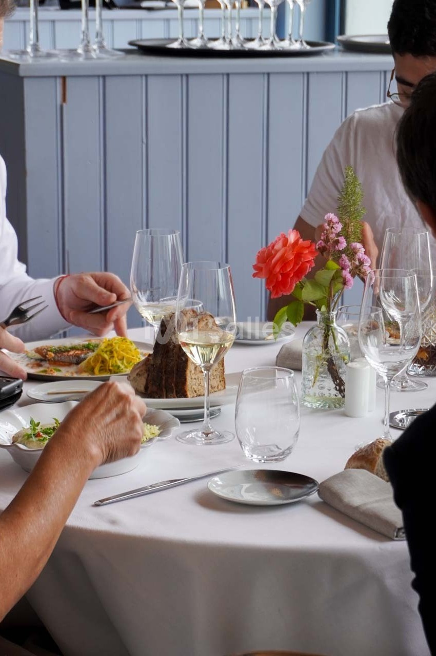 Des convives partagent un repas à une table dressée avec des verres à vin, des fleurs et des plats variés.