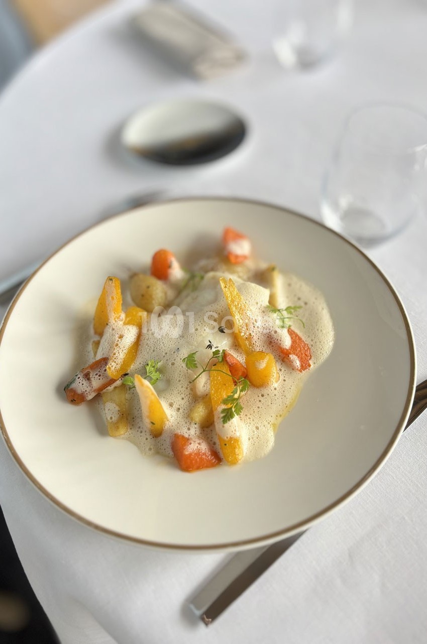 Assiette de légumes colorés nappés d'une mousse légère, présentée sur une table dressée avec élégance.