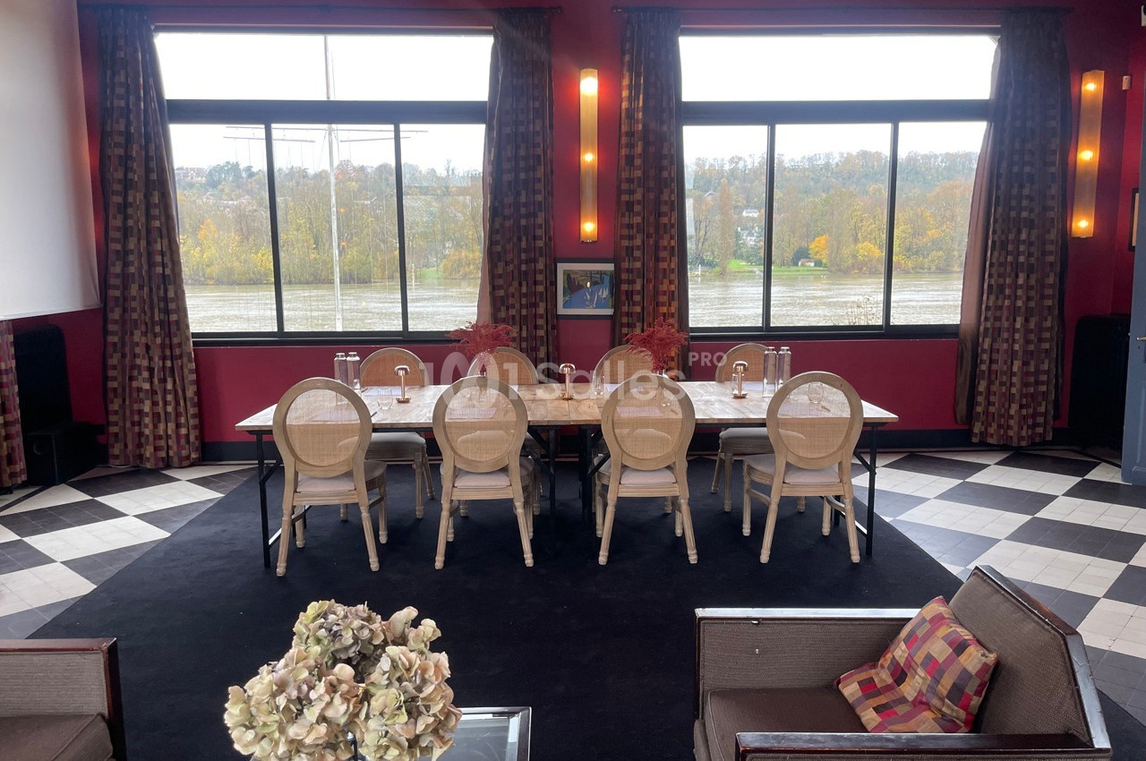 Salle de réunion lumineuse avec une grande table, des chaises en bois clair et des fenêtres donnant sur un paysage automnal.