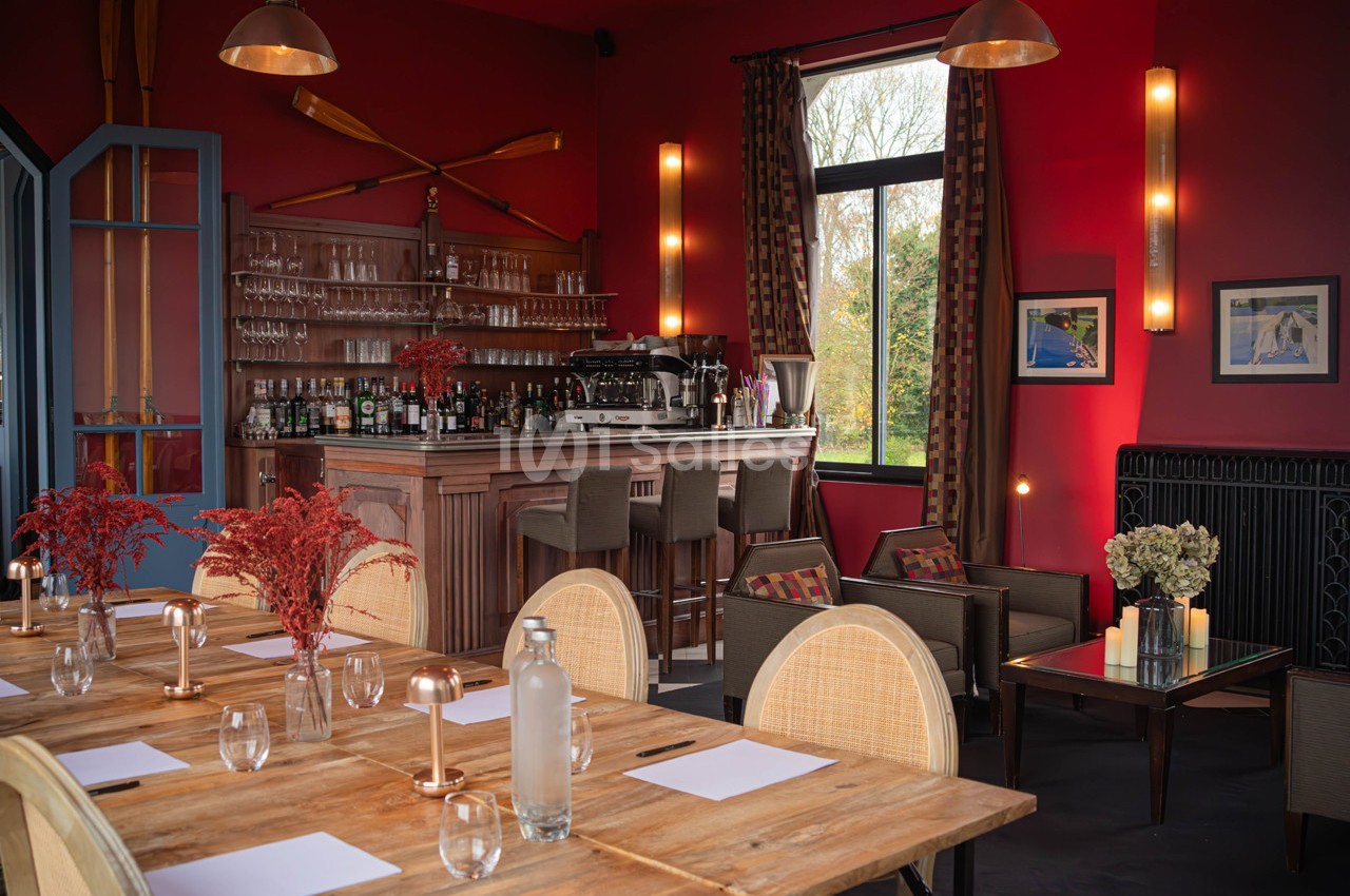Salle de restaurant chaleureuse avec murs rouges, bar en bois, tables dressées et grandes fenêtres donnant sur l'extérieur.