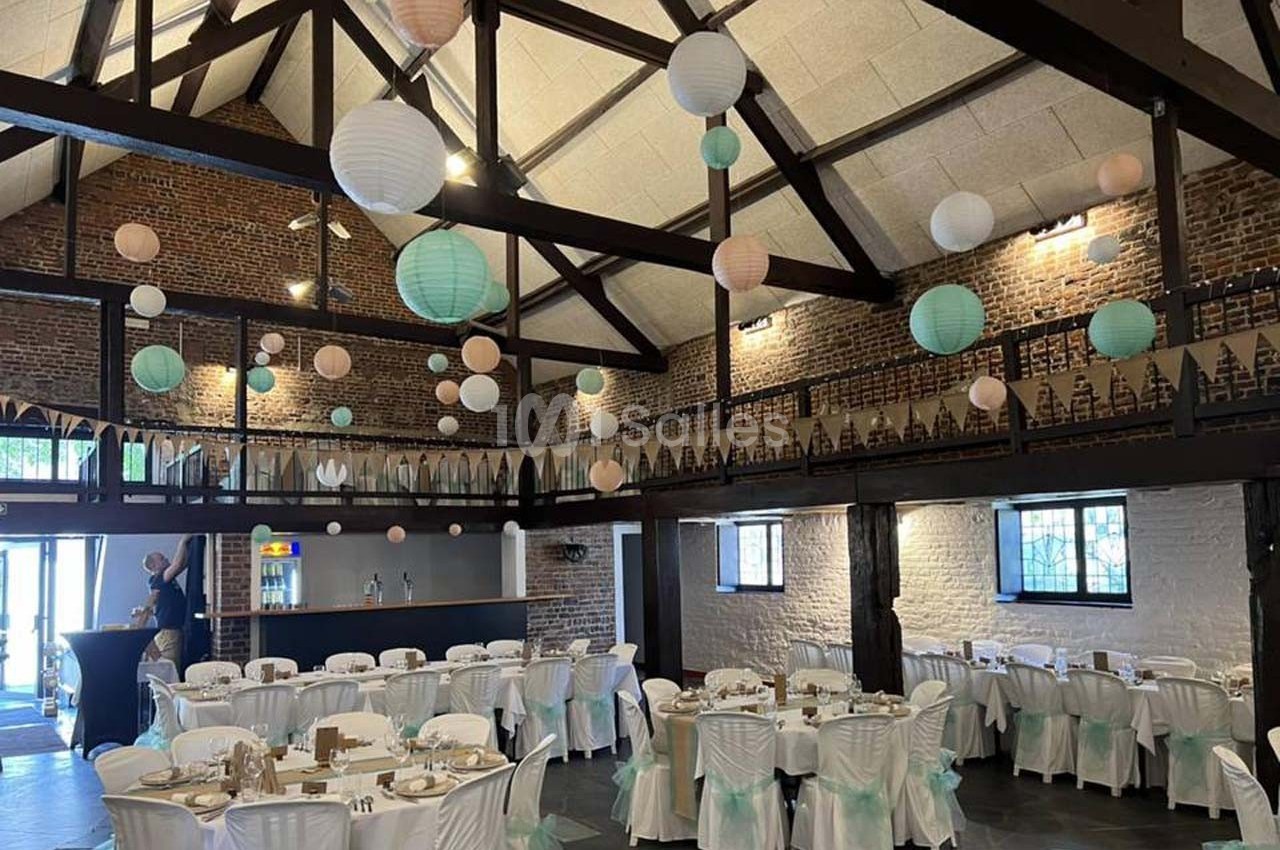 Salle de réception décorée avec des guirlandes, des lanternes suspendues et des tables dressées pour un événement.