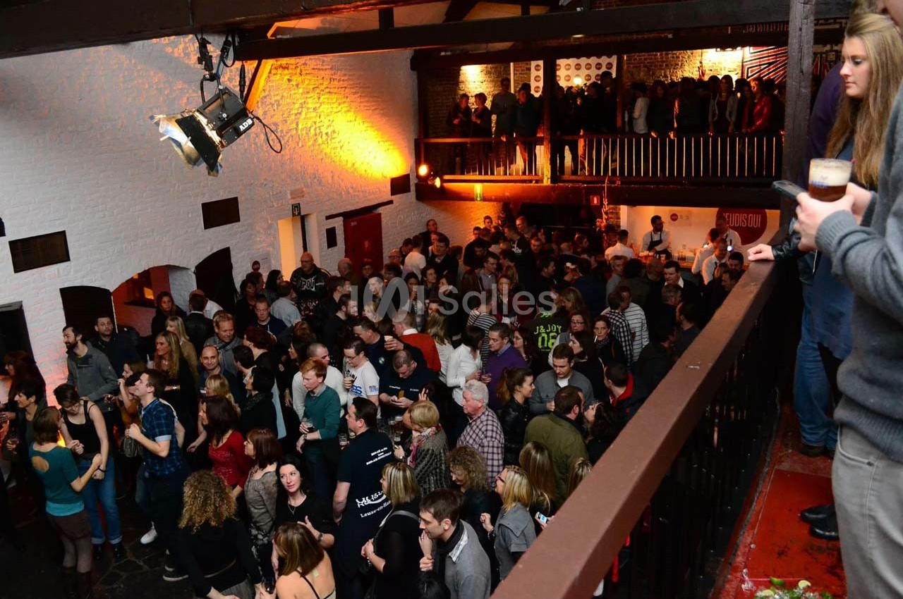 Foule rassemblée dans une salle avec mezzanine, éclairée par des lumières chaudes, lors d'un événement festif.
