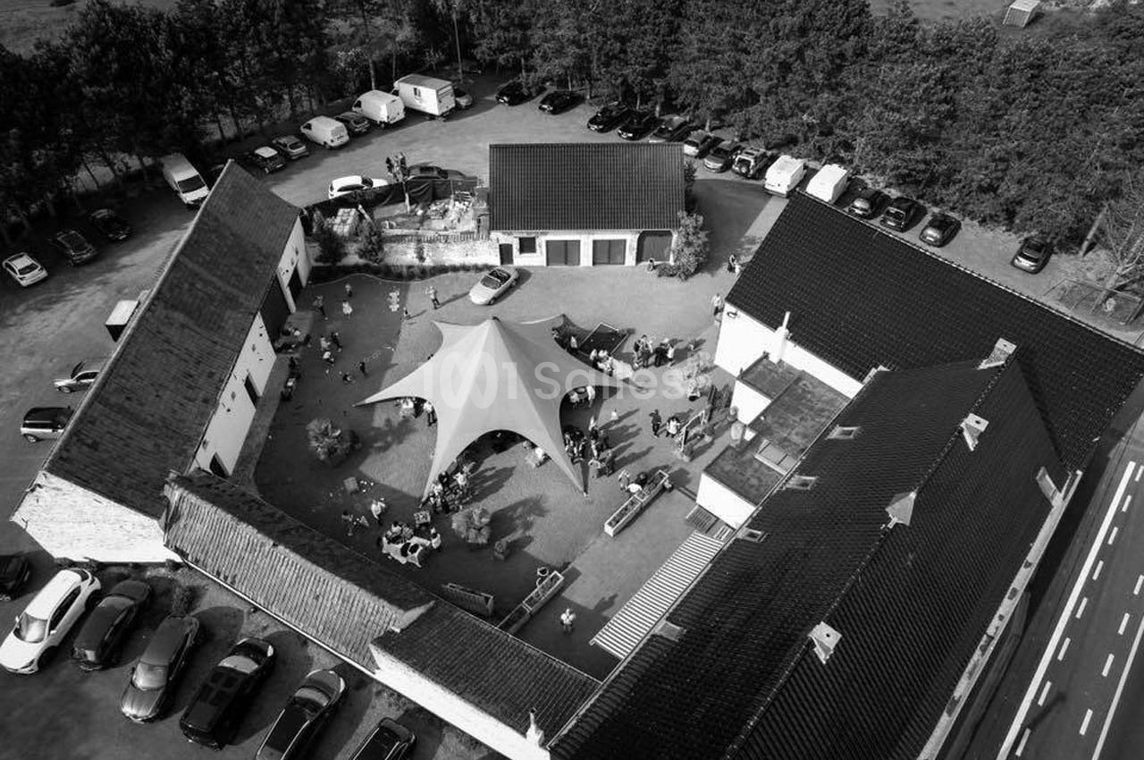Vue aérienne en noir et blanc d'une cour intérieure avec une grande tente, entourée de bâtiments et de voitures.