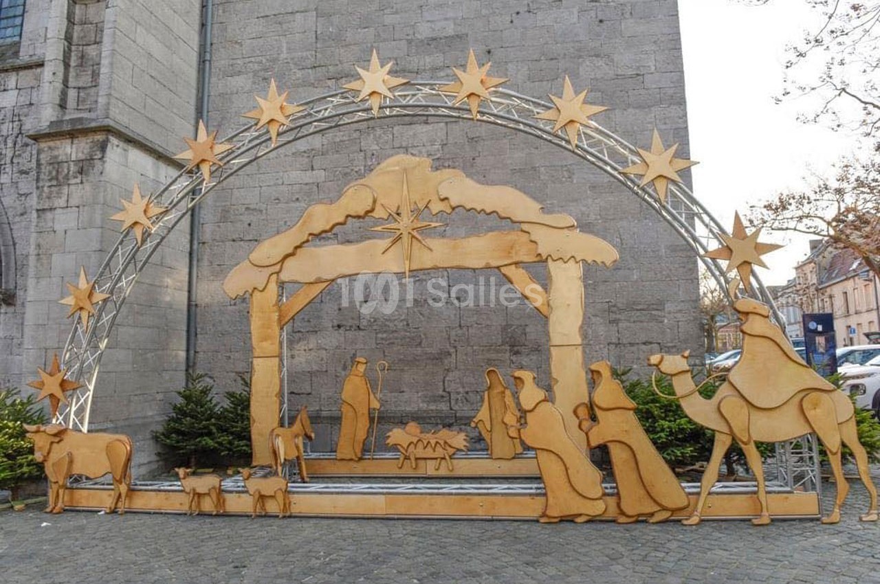 Crèche de Noël en bois avec personnages et animaux sous une arche étoilée, installée devant un mur en pierre.