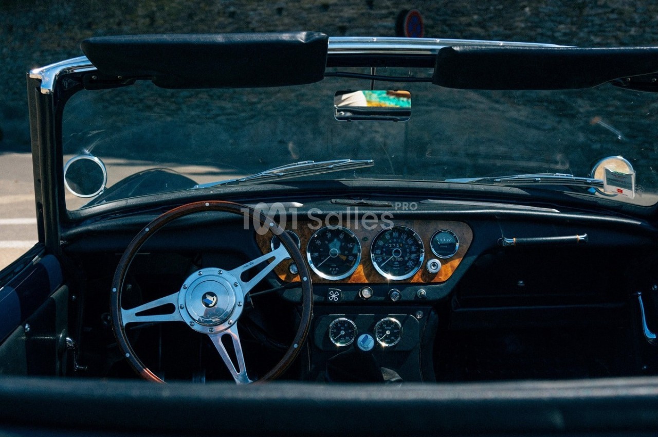 Intérieur d'une voiture ancienne décapotable avec tableau de bord en bois et volant classique.