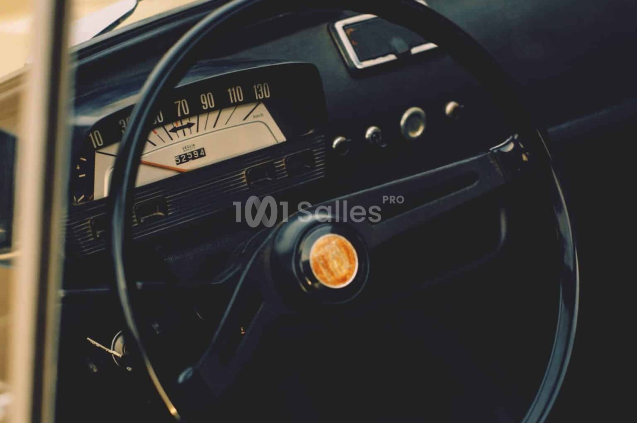 Volant et tableau de bord d'une voiture ancienne avec un compteur de vitesse rétro et des détails noirs.