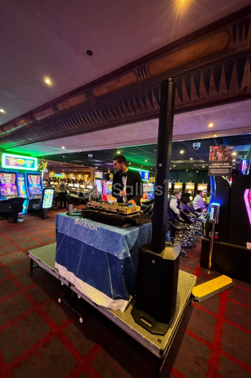Un DJ mixe sur une scène dans un casino, entouré de machines à sous et d'éclairages colorés.