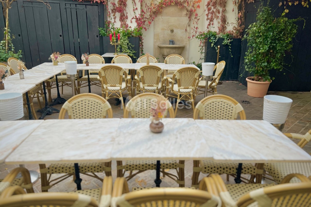 Terrasse aménagée avec des tables en marbre, des chaises en rotin et un mur décoré de plantes grimpantes.