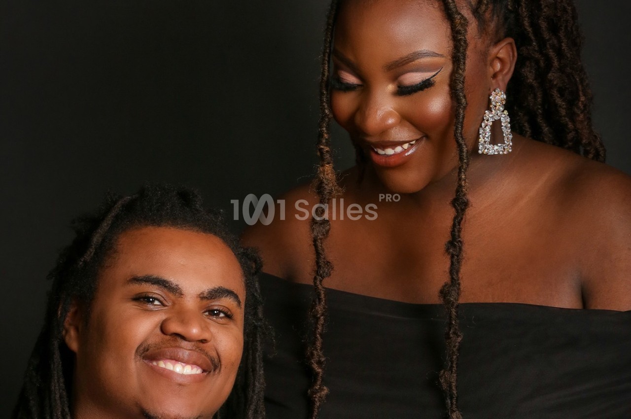 Un homme et une femme souriants, vêtus de noir, posent devant un fond sombre.