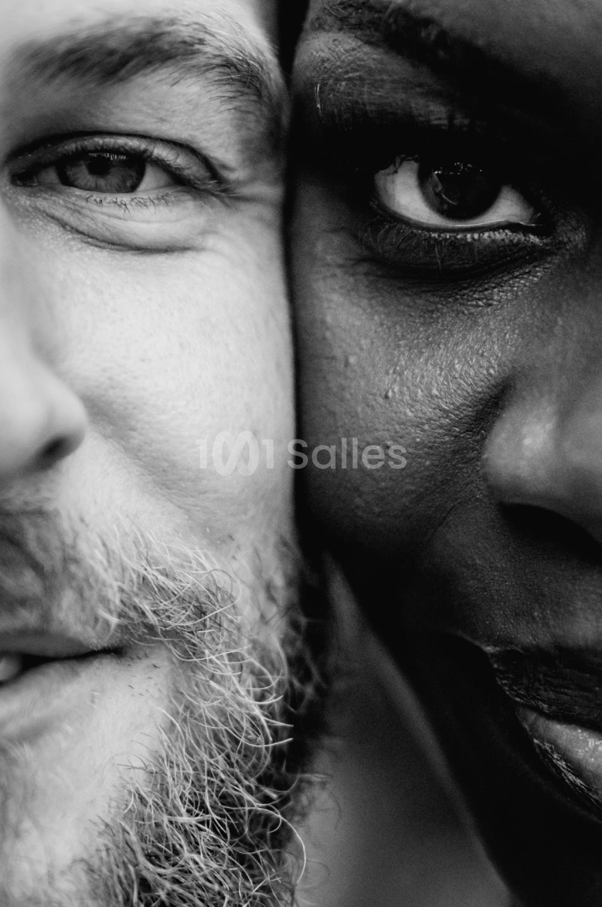 Gros plan en noir et blanc sur les visages partiels d'un homme barbu et d'une femme, leurs regards tournés vers l'objectif.