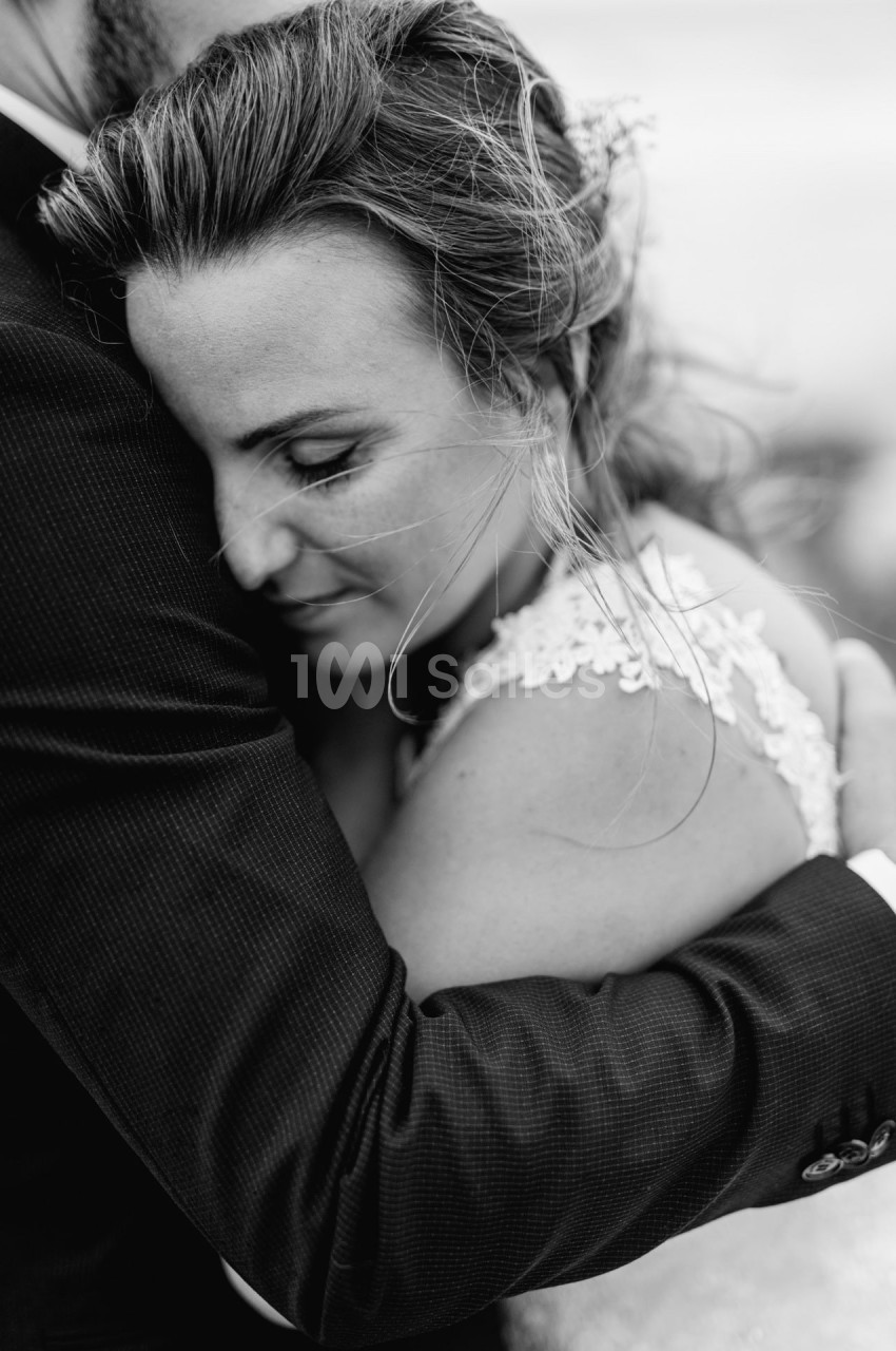 Une femme en robe blanche enlace une personne en costume, exprimant tendresse et émotion.