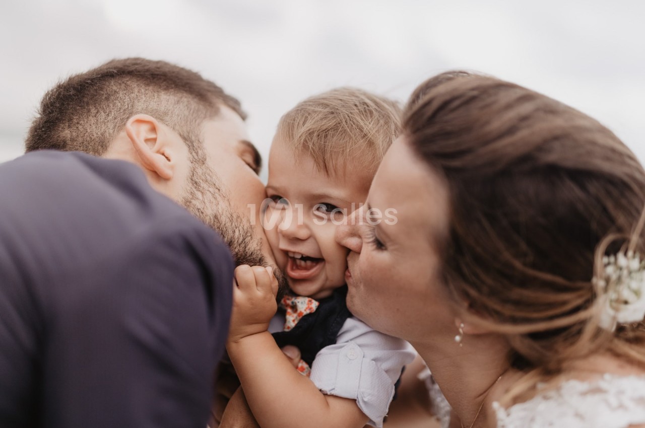 Un couple embrasse tendrement un jeune enfant souriant dans un moment de complicité en extérieur.