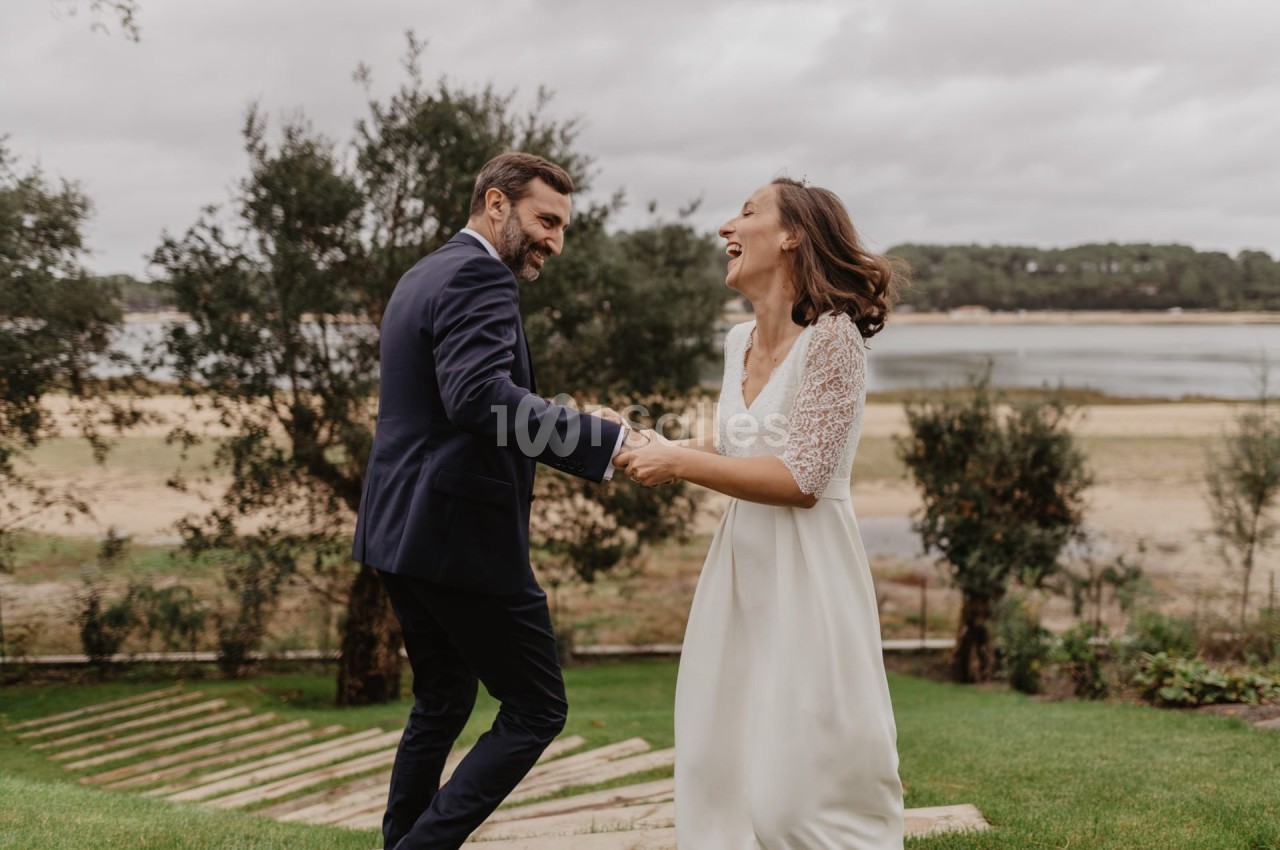 Un couple en tenue de mariage danse joyeusement sur une pelouse avec un paysage naturel en arrière-plan.
