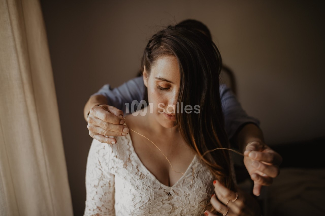 Une personne ajuste un collier autour du cou d'une femme portant une robe en dentelle blanche.