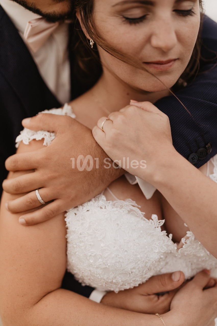 Un couple en tenue de mariage s'enlace tendrement, mettant en valeur leurs alliances.