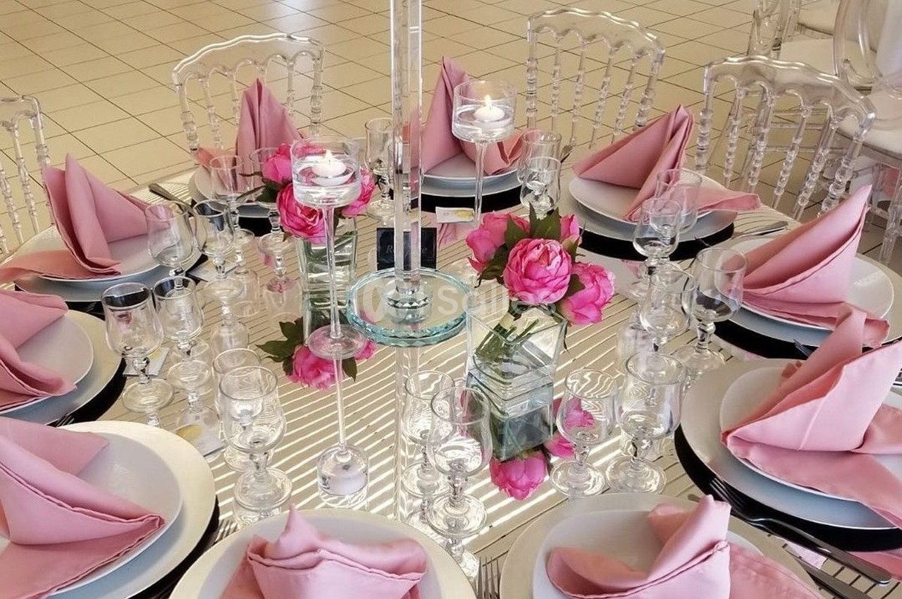 Table ronde élégamment dressée avec des serviettes roses pliées, des verres, des assiettes et un vase de fleurs roses au…