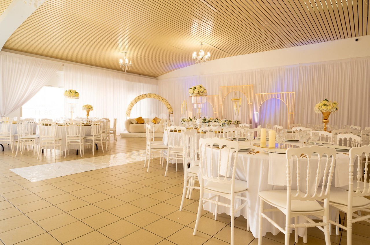 Salle de réception décorée avec des tables rondes, des chaises blanches et des arrangements floraux élégants.